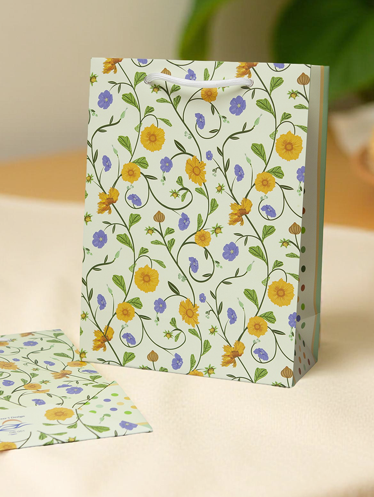 Gift bag with floral pattern of yellow cosmos and blue flax on a pale yellow background. Bag's paper was responsibly sourced.