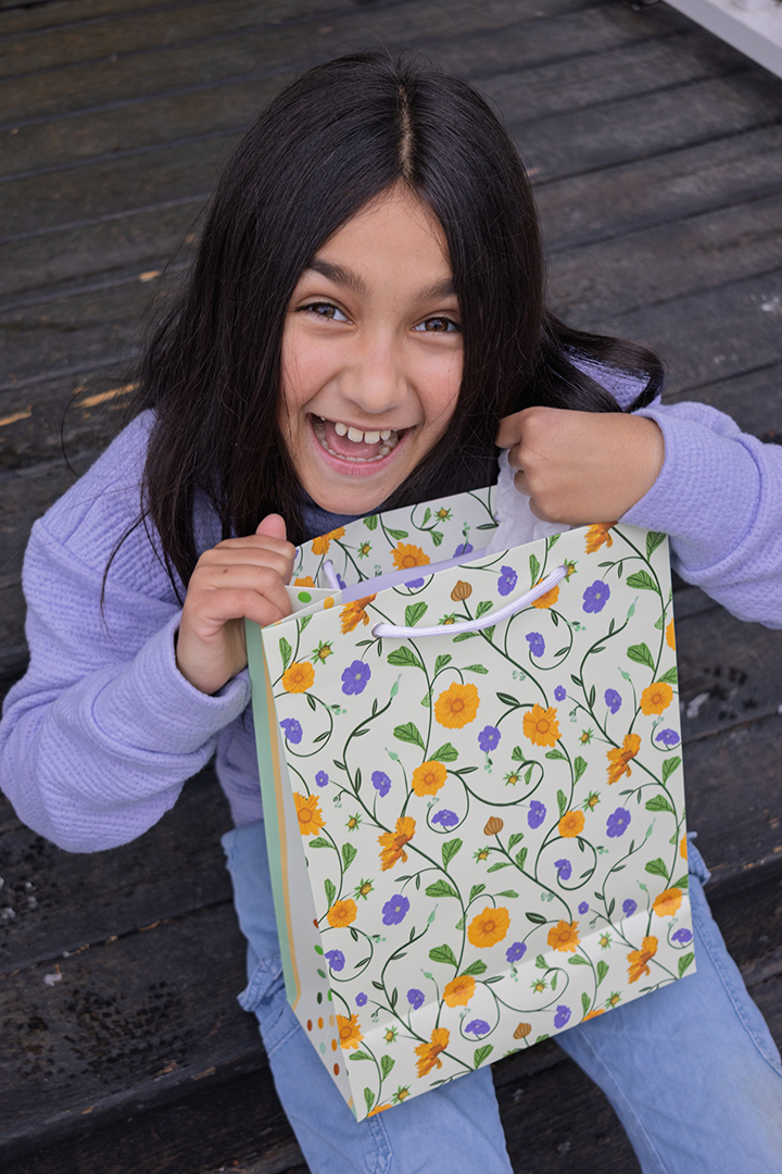Child holding a floral-patterned gift bag on a wooden floor