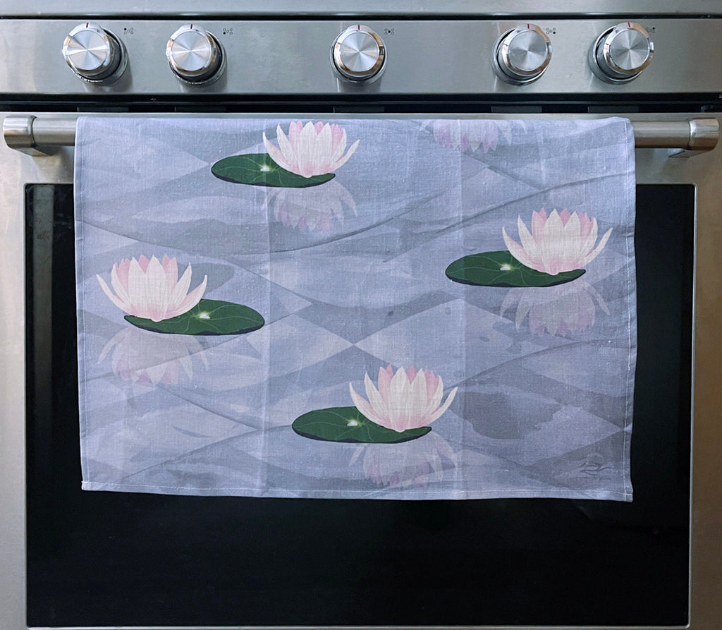 Colorful tea towel hung on an oven handle. Design has water lilies floating in reflective water.